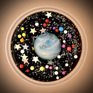 A black slime with a blue and white bouncy ball toy and various colorful beads and silver stars inside a clear plastic container.
