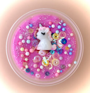 A vibrant pink slime with a white unicorn toy and various colorful beads and sequins inside a clear plastic container.